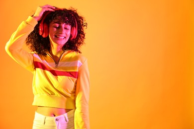 Photo of Beautiful young woman listening to music with headphones on color background in neon lights. Space for text