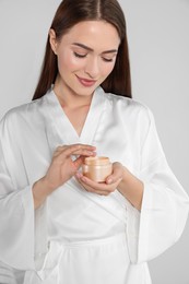 Photo of Smiling woman taking hand cream from jar on light background