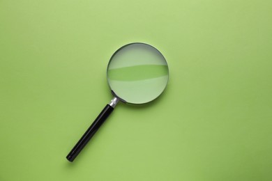 Photo of Magnifying glass on light green background, top view