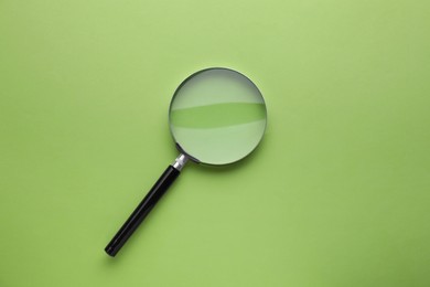 Magnifying glass on light green background, top view