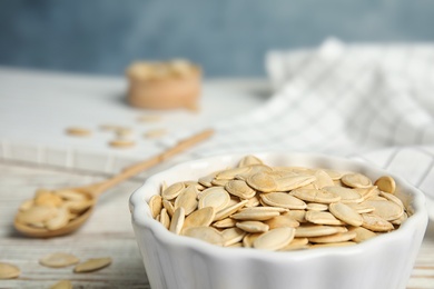 Photo of Bowl of raw pumpkin seeds on white wooden table, closeup. Space for text