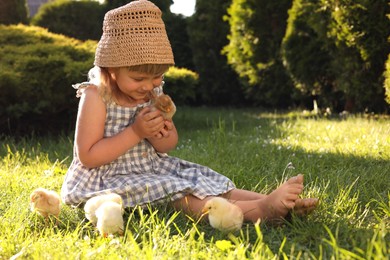 Photo of Little girl with cute chicks on green grass outdoors. Baby animals