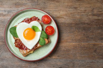 Photo of Tasty sandwich with heart shaped fried egg and  bacon on wooden table, top view. Space for text