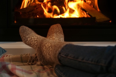 Photo of Woman in warm socks resting near fireplace at home, closeup