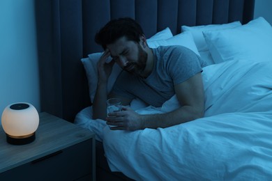 Photo of Man with glass of water suffering from headache in bed at night