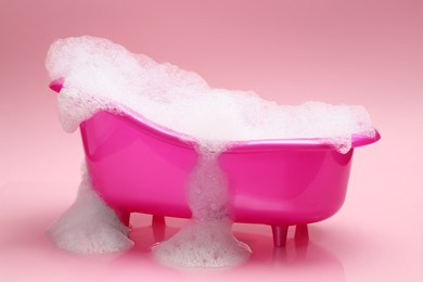 Photo of Toy bathtub overflowing with foam on pink background