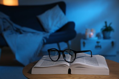 Photo of Book and glasses on wooden coffee table indoors at night