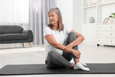 Photo of Senior woman sitting on mat at home. Yoga practice