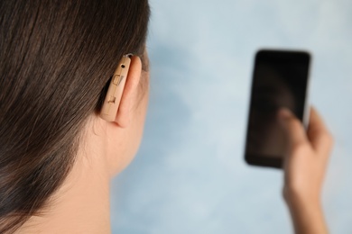Photo of Patient with hearing aid and smartphone on light background, closeup. Space for text