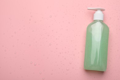 Photo of Wet bottle of face cleansing product on pink background, top view. Space for text