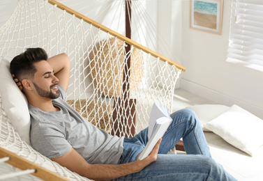 Photo of Young man reading book in hammock at home