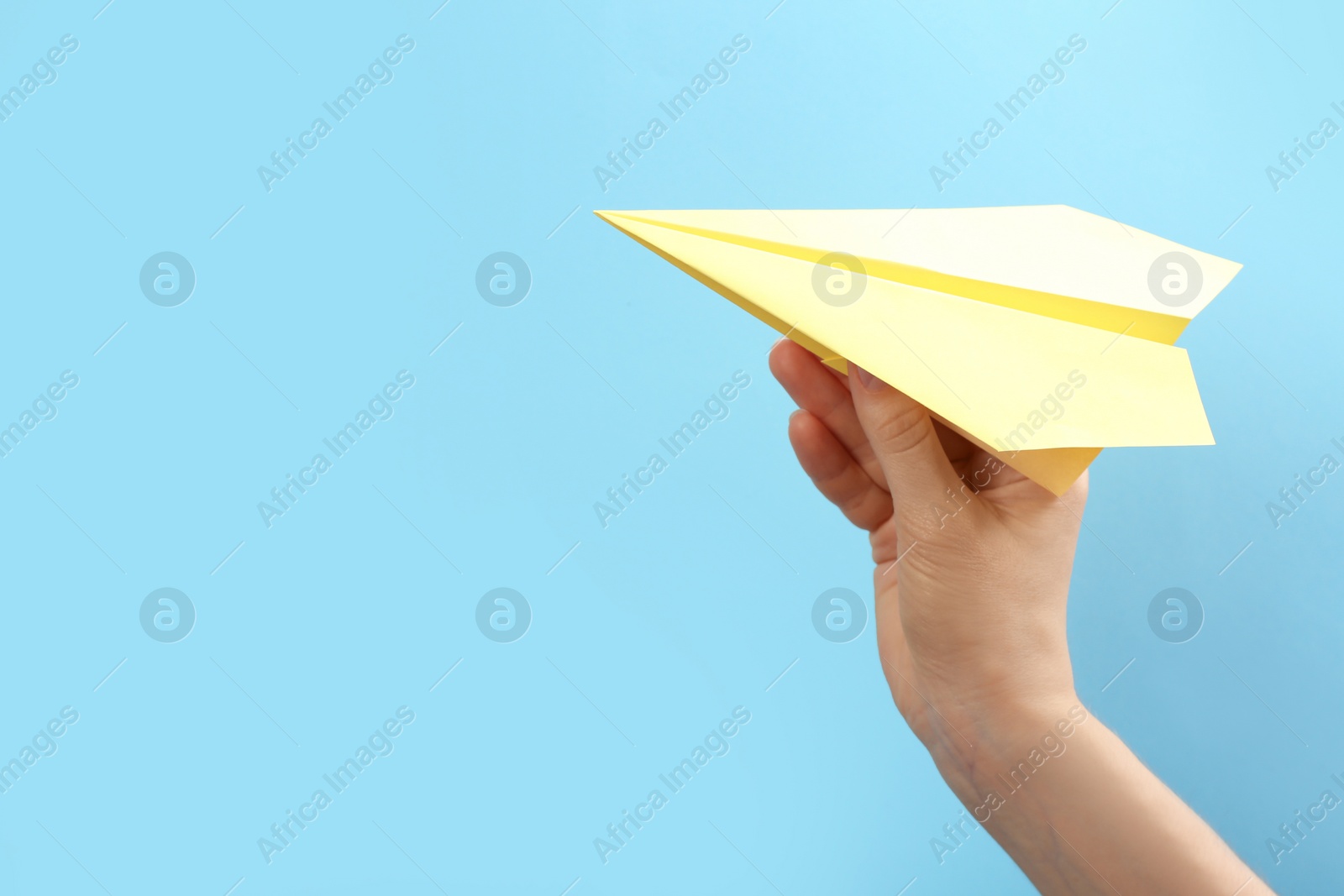 Photo of Woman holding paper plane on light blue background, closeup. Space for text