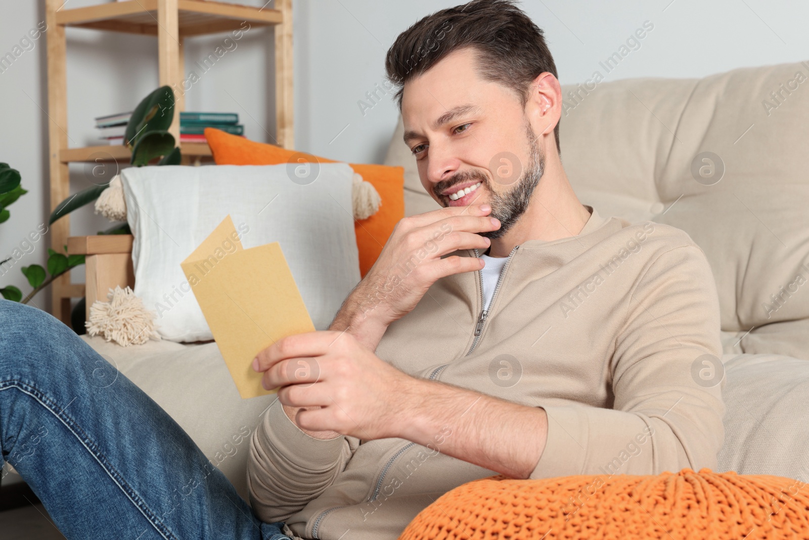 Photo of Happy man reading greeting card on sofa in living room