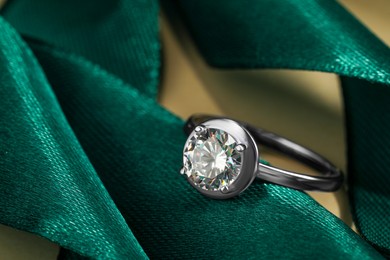 Photo of Beautiful luxury engagement ring with gemstone on green ribbon, closeup
