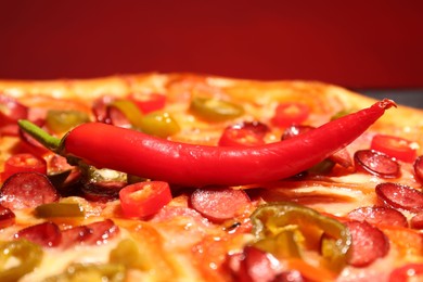 Photo of Delicious pizza Diablo and chili pepper against red background, closeup