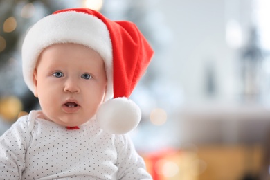 Photo of Little baby wearing Santa hat indoors. First Christmas