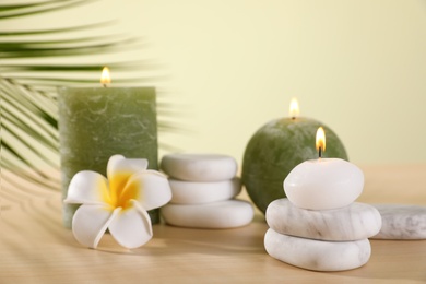 Photo of Composition of spa stones and burning candles with flower on wooden table against light green background