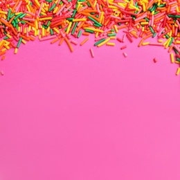 Photo of Bright colorful sprinkles on pink background, flat lay with space for text. Confectionery decor