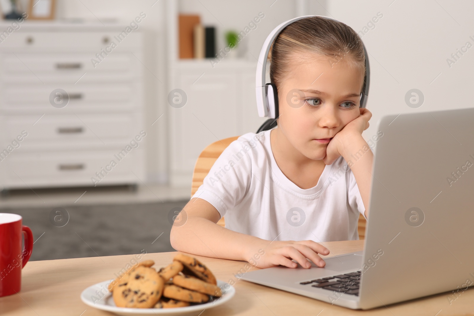 Photo of Little girl in headphones using laptop at table indoors, space for text. Internet addiction