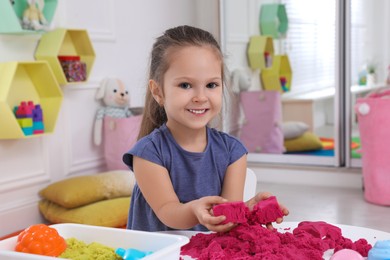 Photo of Cute little girl playing with bright kinetic sand at table in room
