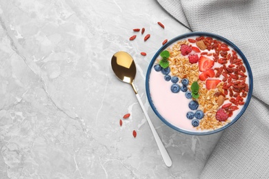 Photo of Smoothie bowl with goji berries and spoon on grey table, flat lay. Space for text