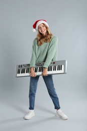 Photo of Young woman in Santa hat with synthesizer on light grey background. Christmas music