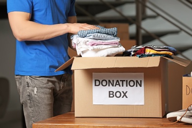 Photo of Male volunteer putting clothes in donation box indoors