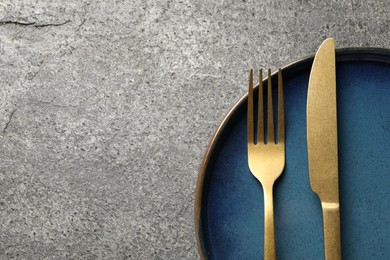 Photo of Stylish golden cutlery and plate on grey table, top view. Space for text