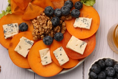 Photo of Delicious persimmon with blue cheese on white wooden table, flat lay