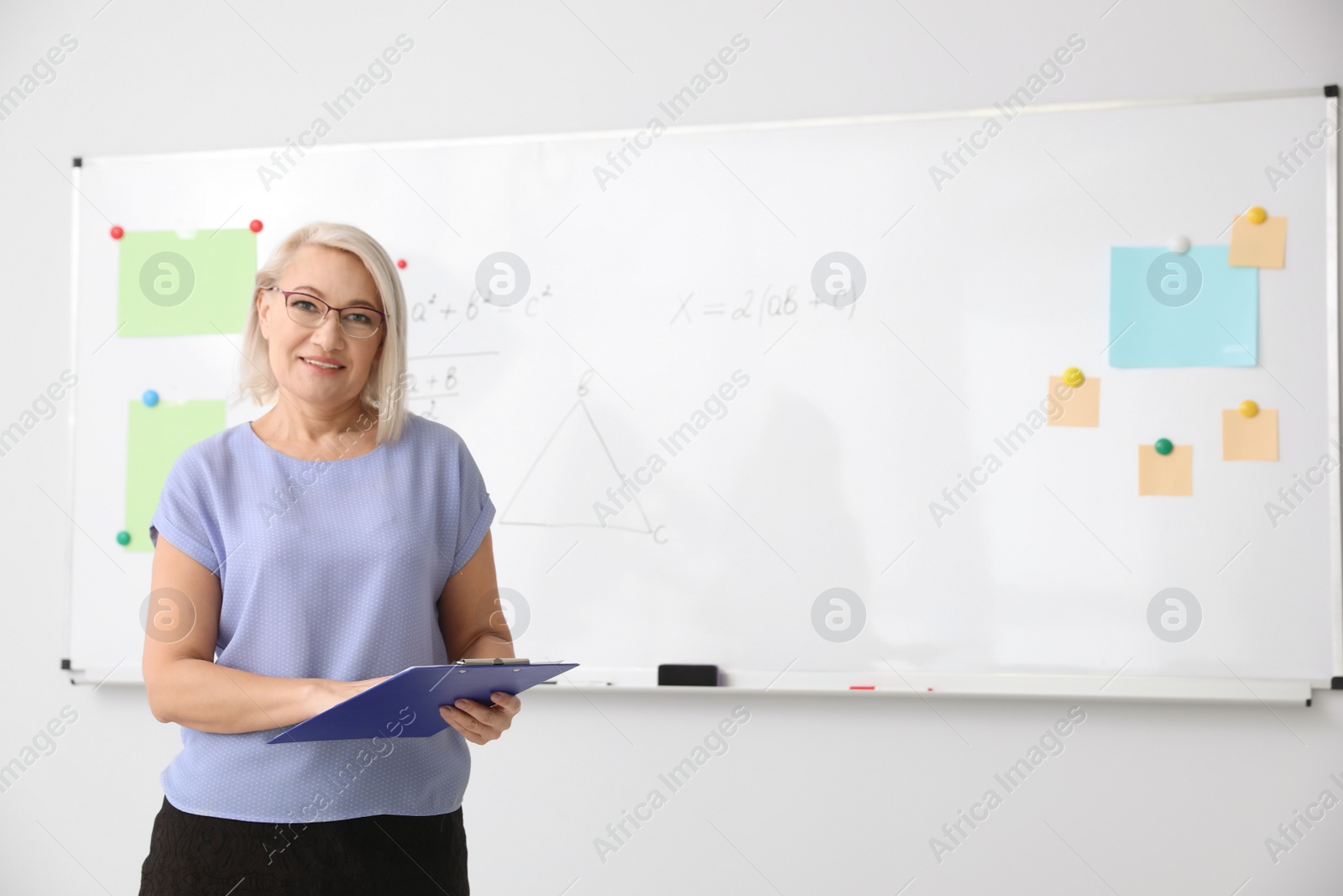 Photo of Mature teacher with clipboard near whiteboard in modern classroom. Space for text