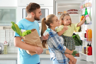 Photo of Happy family putting products into refrigerator in kitchen