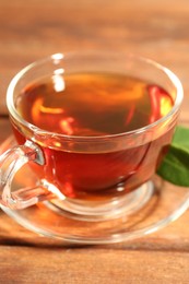 Photo of Aromatic tea in glass cup and green leaves on wooden table, closeup
