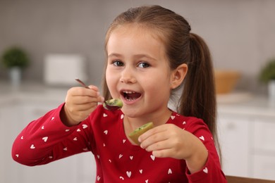 Photo of Cute girl eating tasty fresh kiwi indoors