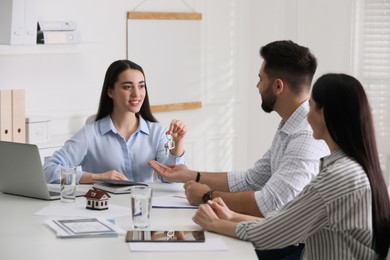 Photo of Real estate agent giving house key to young couple in office. Mortgage concept