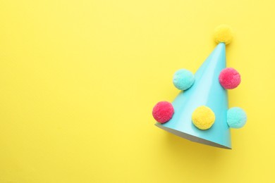 Photo of One light blue party hat with pompoms on yellow background, top view. Space for text