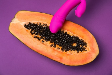 Photo of Half of papaya and vibrator on purple background, top view. Sex concept