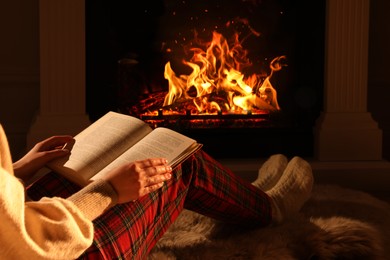 Photo of Woman with book near fireplace at home, closeup