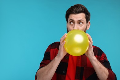 Photo of Man inflating yellow balloon on light blue background. Space for text