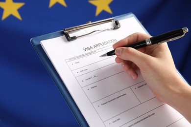 Photo of Woman filling visa application form against flag of European Union, closeup