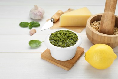 Photo of Delicious pesto sauce in bowl and ingredients on white wooden table. Space for text
