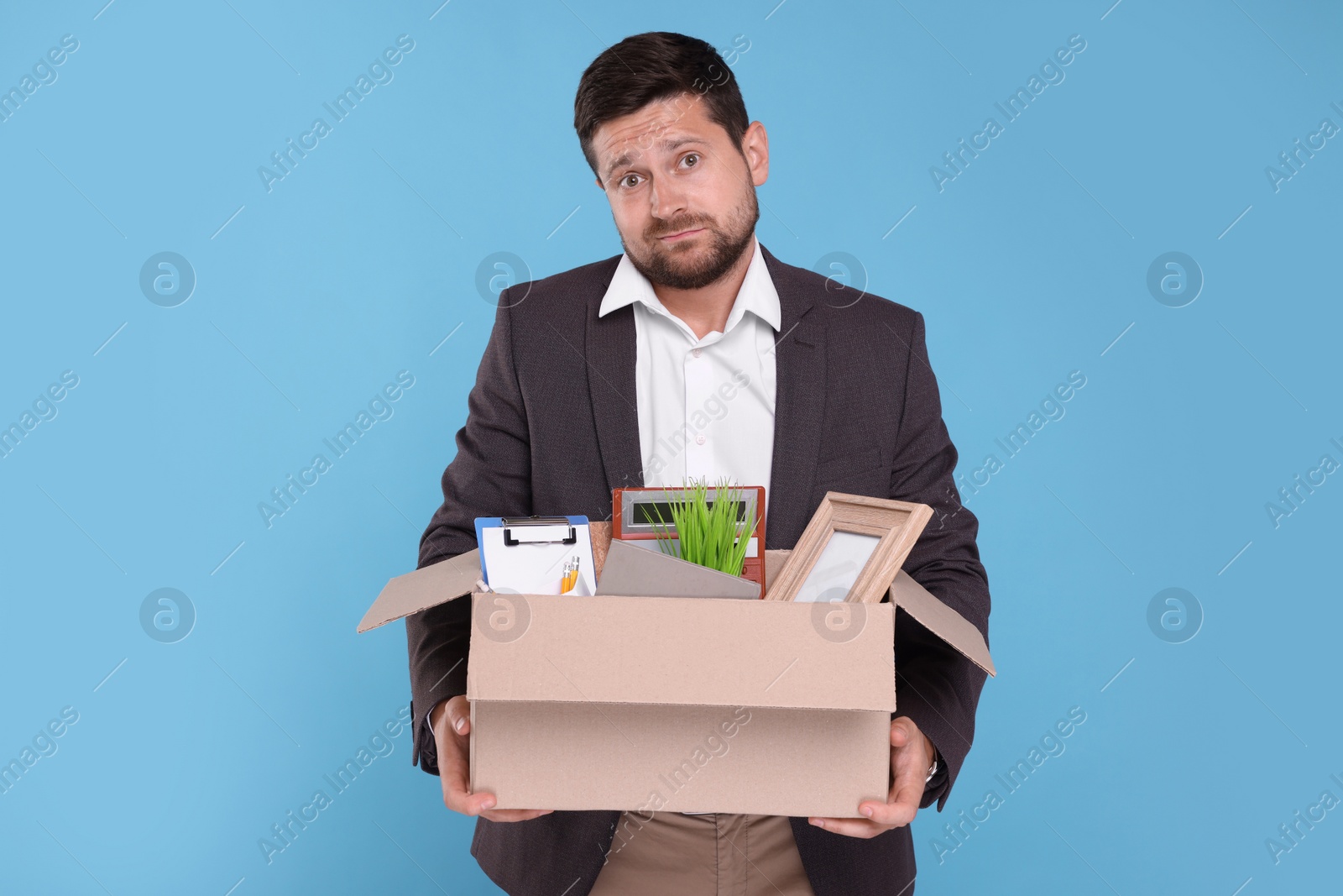 Photo of Unemployed man with box of personal office belongings on light blue background