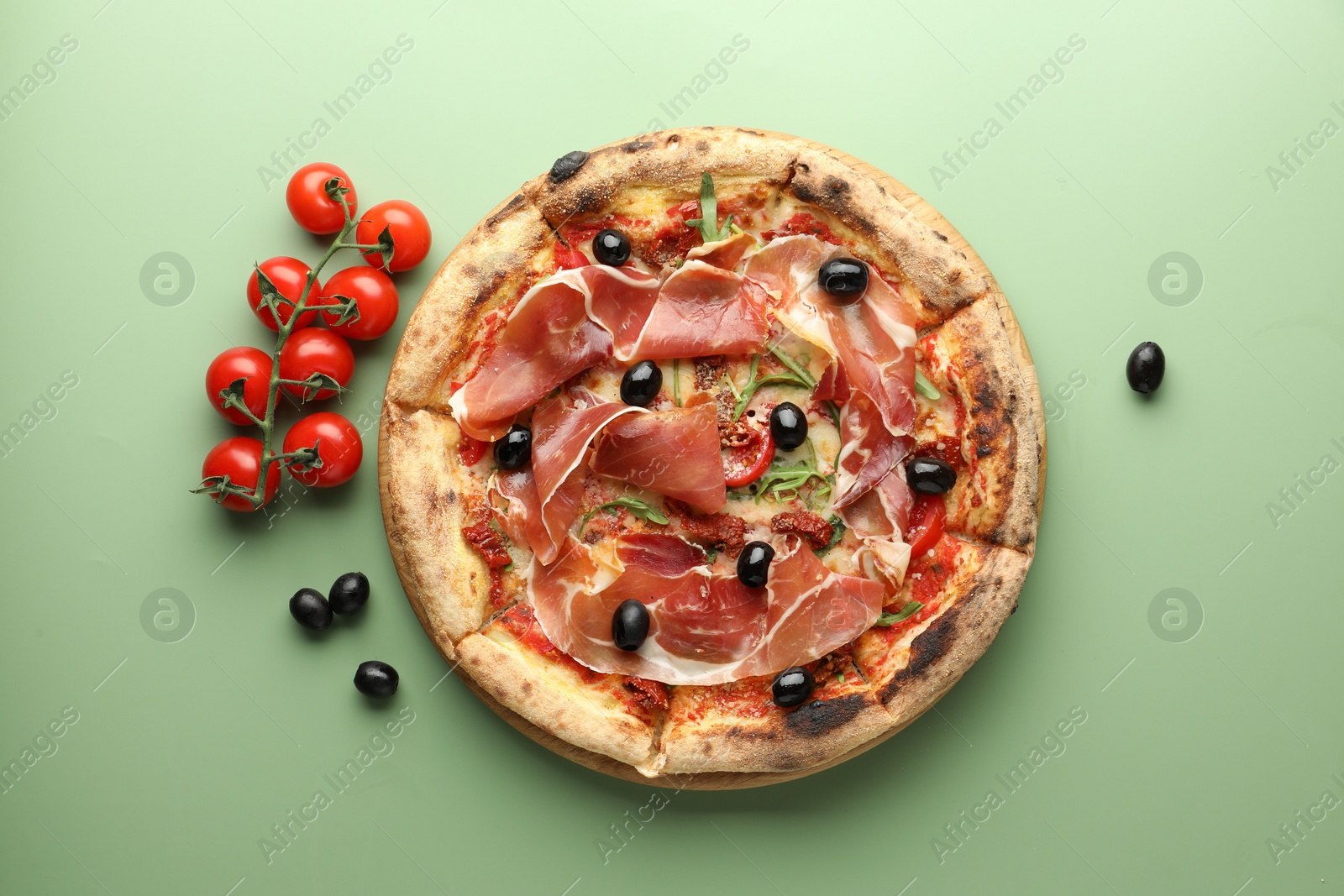 Photo of Tasty pizza with cured ham, olives and tomatoes on green background, top view