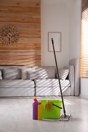 Photo of Floor mop, cleaning detergents and bucket with gloves in living room