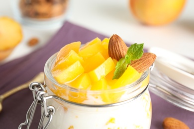 Photo of Tasty peach dessert with yogurt in glass jar on table, closeup