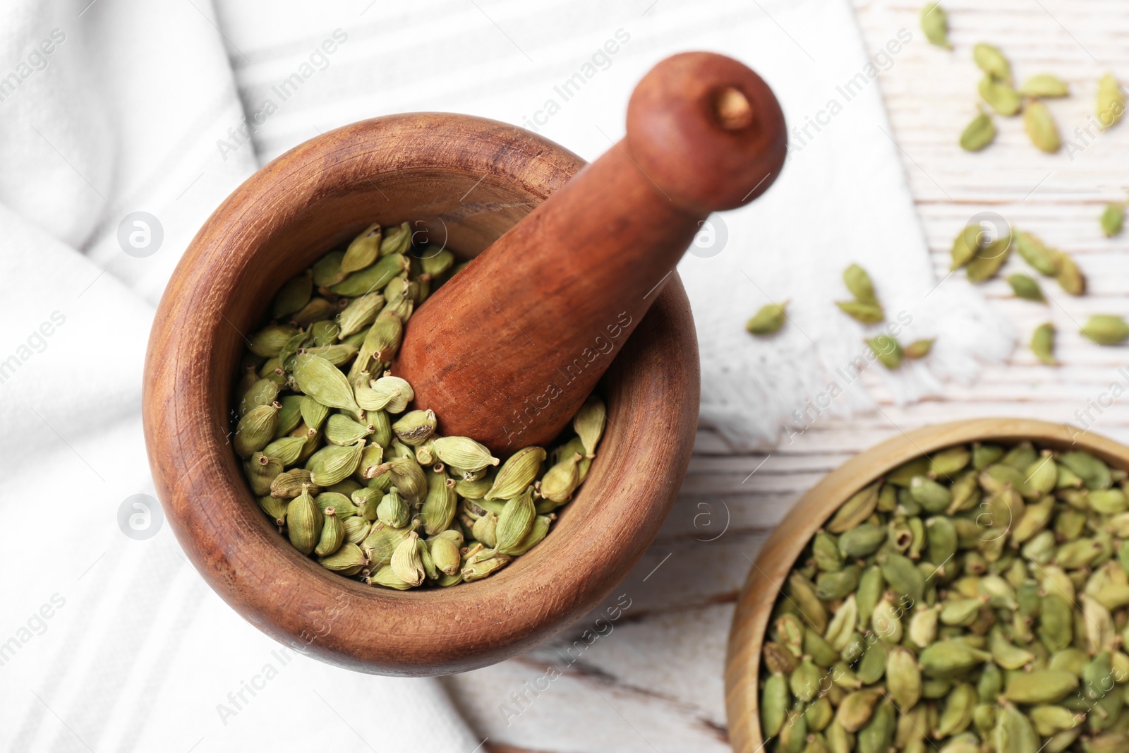 Photo of Mortar and pestle with dry cardamom on wooden table, flat lay