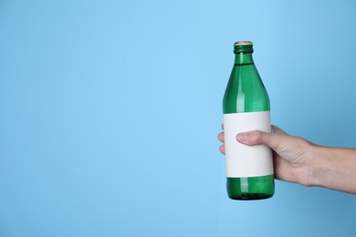 Photo of Woman holding glass bottle with soda water on light blue background, closeup. Space for text