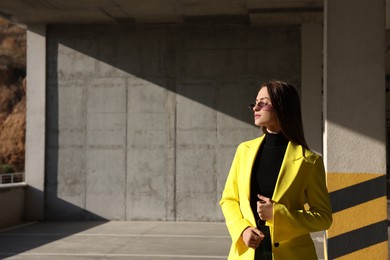Photo of Fashionable young woman wearing stylish outfit with yellow jacket in open parking garage. Space for text