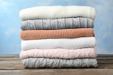Photo of Stack of warm clothes on wooden table against light blue background. Autumn season