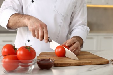 Photo of Professional chef cutting tomatoes at white marble table indoors, closeup