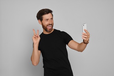 Photo of Happy man taking selfie on smartphone against light background